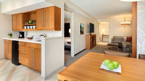A modern kitchen with wooden cabinets, a black refrigerator, and a dining area with a wooden table and a plate of green apples. - Hyatt Place Vacaville (Vacaville)
