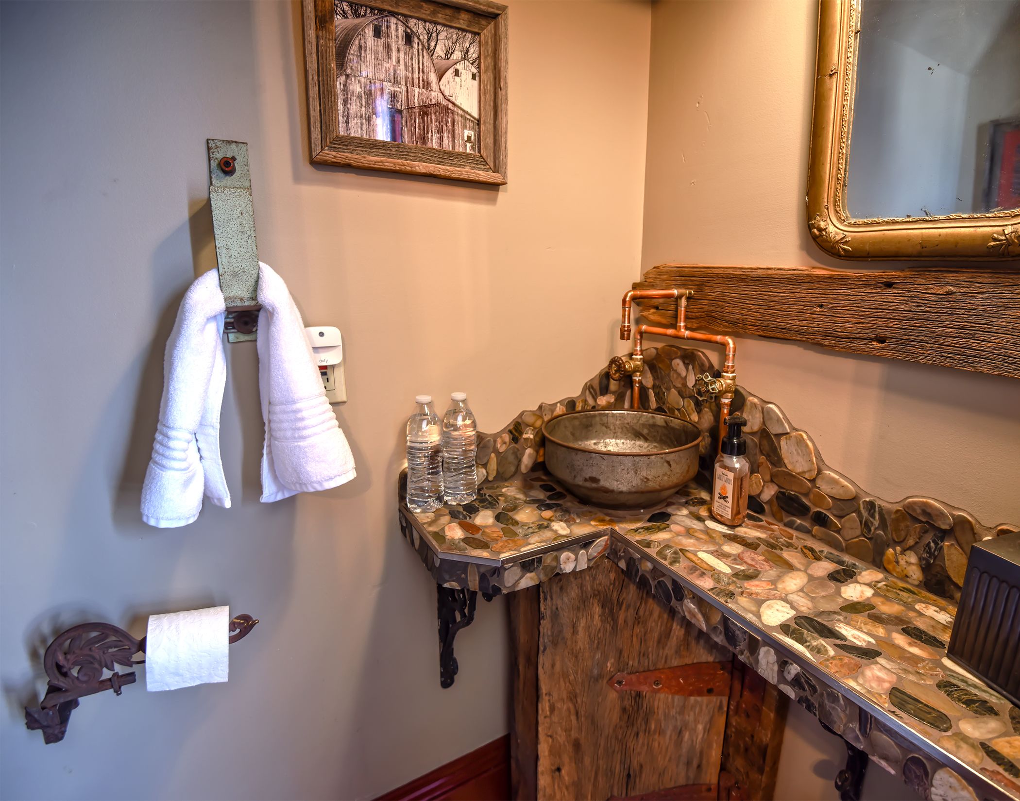 A bathroom with a rustic stone sink, a mirror with a wooden frame, and towels hanging on a rack.