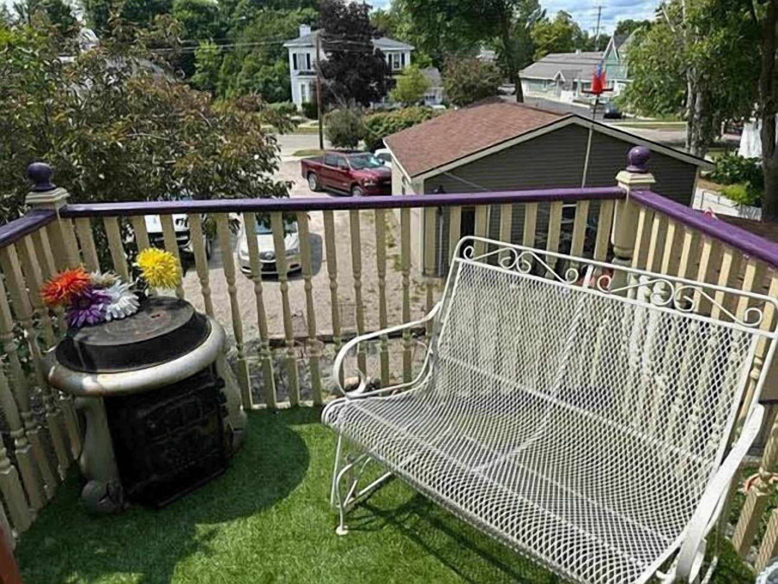 A balcony with a white metal bench, a small table with flowers, and a grill.