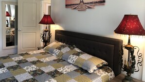 Une chambre à coucher avec un lit, deux lampes, une porte et un tableau représentant la Tour Eiffel accroché au mur.