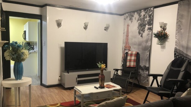 Un salon moderne avec un téléviseur à écran plat, une table basse, un canapé et un fauteuil. On trouve un vase décoratif sur la table basse et un tableau au mur.
