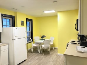 Una cocina compacta con una pared amarilla, un refrigerador blanco, una mesa de comedor con sillas y una estufa.