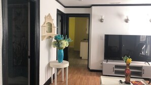 Un salon comprenant un téléviseur, un meuble blanc, une petite table avec un vase et un élément décoratif mural.