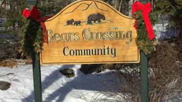 Un panneau en bois orné d’un dessin d’un ours et d’une montagne, portant l’inscription « Bears Crossing Community », et surmonté de nœuds rouges.
