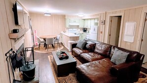Un espacio habitable compacto con un sofá de cuero marrón, una mesa de comedor con sillas, una zona de cocina y una chimenea.