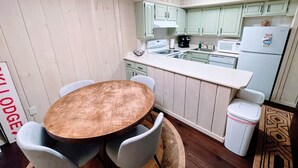 Una cocina compacta con una mesa y sillas de madera, una encimera blanca y armarios de color verde claro.