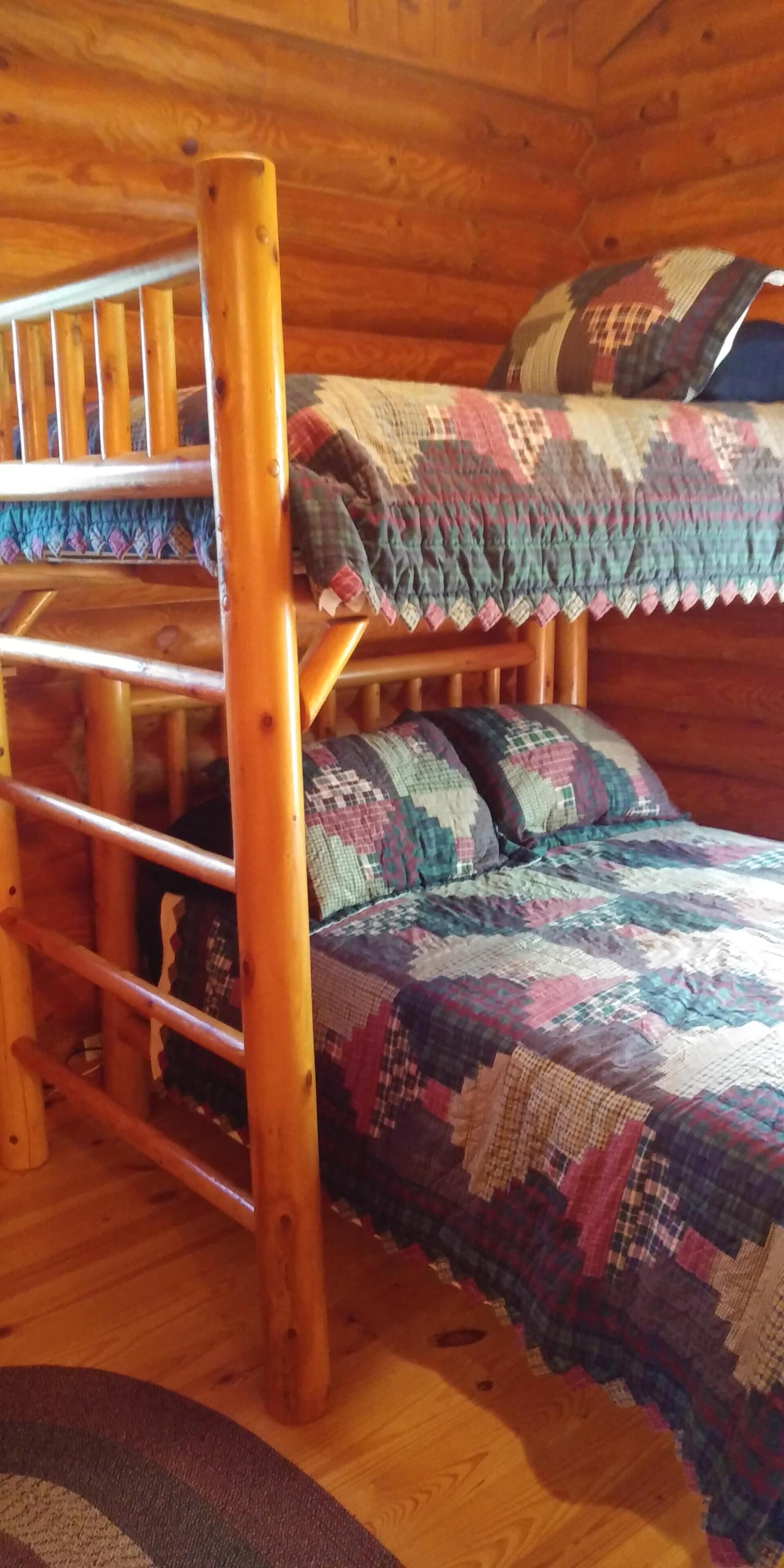 Een houten stapelbed met een kleurrijke sprei, een houten trap en een geruite plaid op het bed.