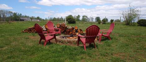 Eine Gruppe roter Adirondack-Stühle ist um eine Feuerstelle in einer grünen Außenanlage angeordnet.