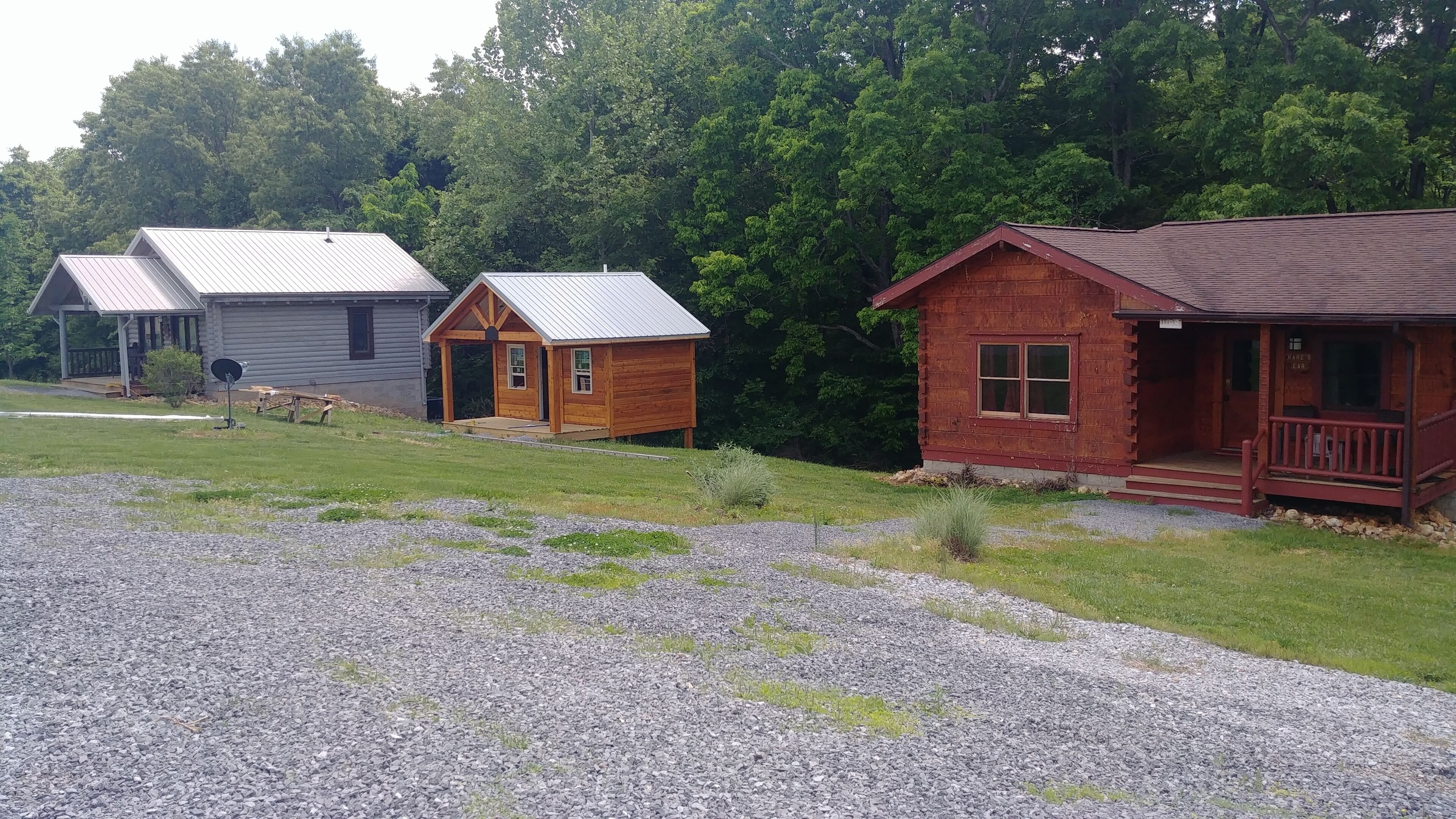Three cabins with metal roofs, a gravel driveway, and a grassy area.