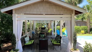 A covered patio with outdoor furniture, a grill, and a pool in the background. - NEW RESORT-STYLE POOL, CUTE HOUSE, 88 STEPS TO SAND! (Hilton Head Island)