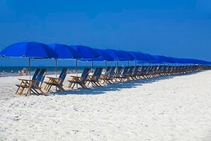A beach with rows of blue umbrellas and wooden lounge chairs.