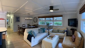 A spacious living room with a white sofa, a smaller sofa, and a brown leather chair. There is a dining area with a wooden table and chairs, and a TV mounted on the wall. - NEW RESORT-STYLE POOL, CUTE HOUSE, 88 STEPS TO SAND! (Hilton Head Island)