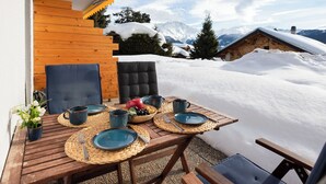 Een houten tafel gedekt met borden, bekers en een fruitschaal, met uitzicht op een besneeuwd berglandschap.