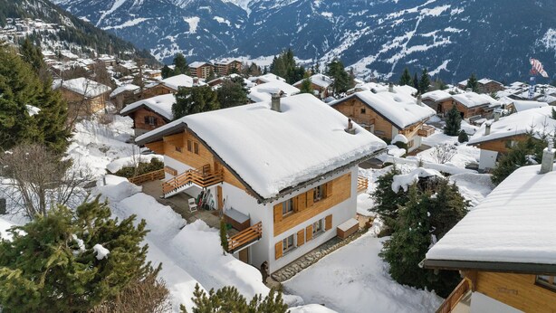 Een besneeuwde bergdorp met houten huizen, een stenen pad en een uitzicht op besneeuwde bergtoppen.