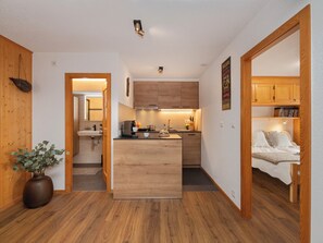 A compact kitchen with wooden cabinets, a central island, and a sink. There is a potted plant and a wooden floor.