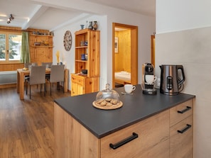 Una cocina acogedora con armarios de madera, un comedor con sillas, una cafetera y vistas a una habitación de madera.