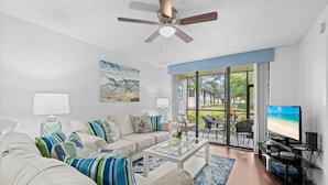 A living room with a sofa, coffee table, TV, and a balcony with a view of the beach. - *Casa Mia* Fabulous 2BR Condo w/2Pools, Mins to IMG/Beach/Anna Maria Isl (Bradenton)