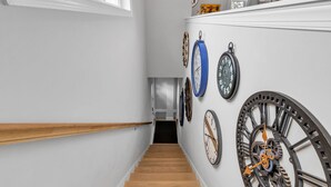 Una escalera de madera con barandilla que lleva a un rellano con una pared blanca y un reloj.