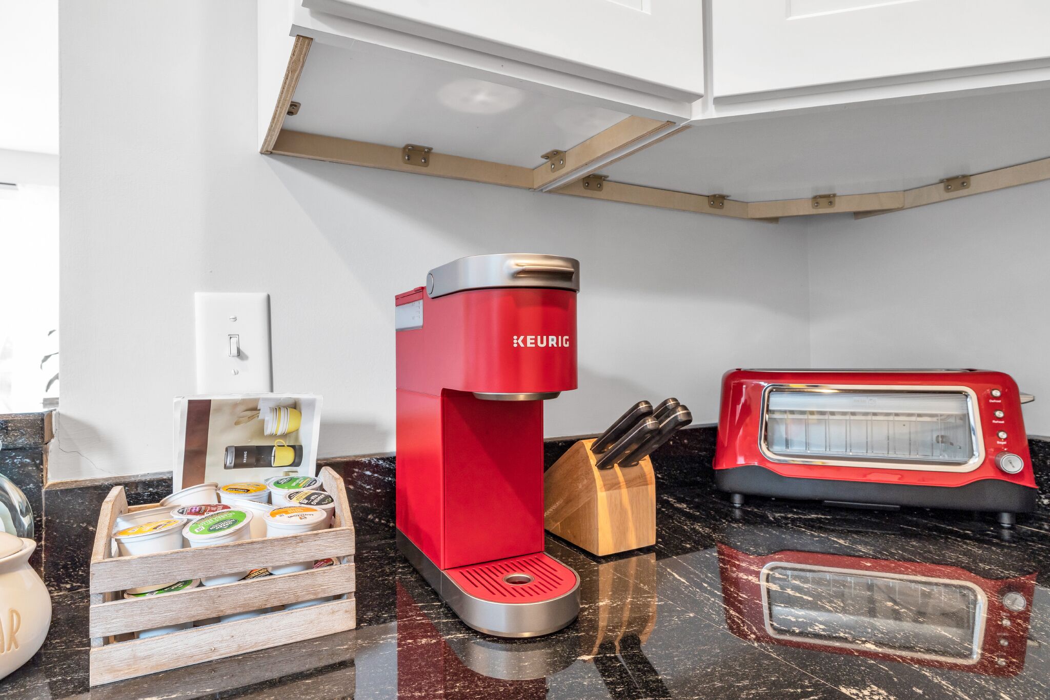 Eine Küche mit einem roten Keurig-Kaffeemaschine, einem Toaster und einem Holz-Utensilienhalter auf einer Marmarbeitung.