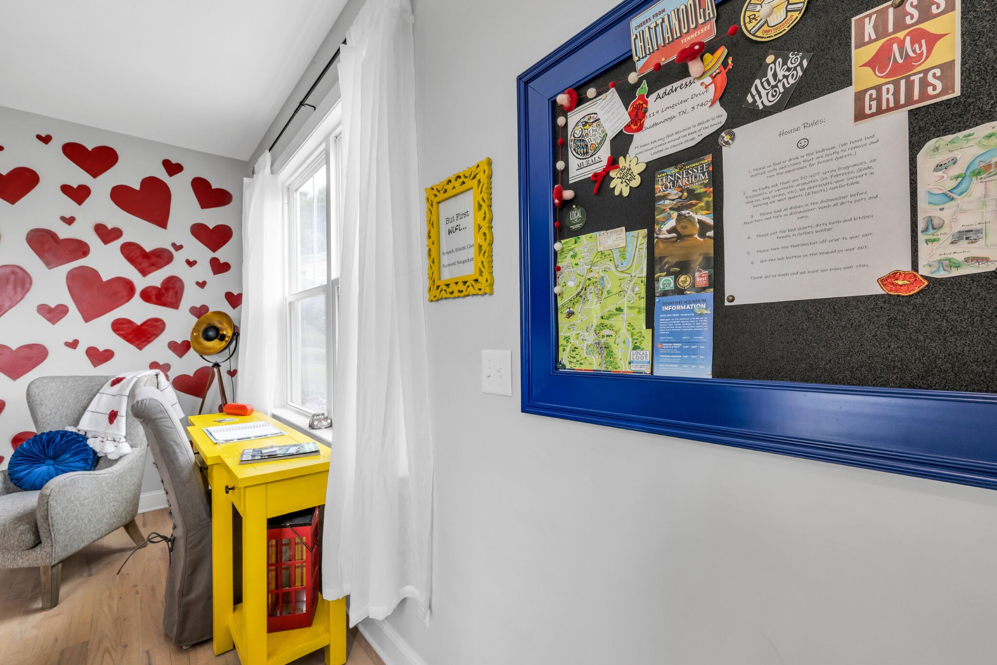 A room with a bulletin board, a chair, a small table, and a wall decorated with red hearts.