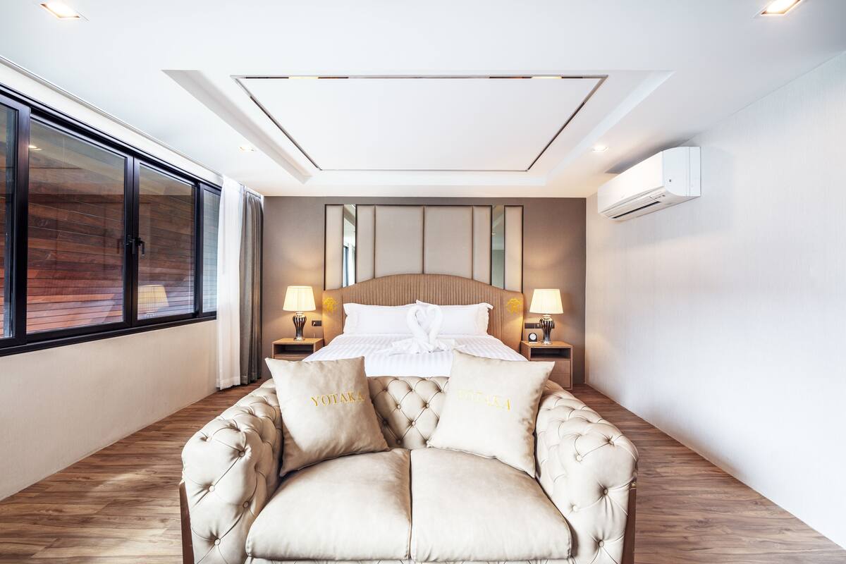 A modern bedroom with a large bed, two bedside tables with lamps, a tufted armchair, and a large window.