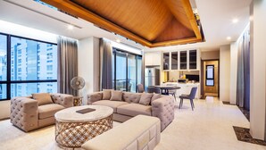 A modern living room with a sectional sofa, a round coffee table, and a dining area with a table and chairs. - Grand Sala Thai (Bangkok)