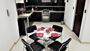 A compact kitchen with black cabinets, a dining table set for four, and a microwave. - Departamentos Arequipa Inn (Arequipa)