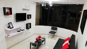 A modern living room with a black sofa, a glass coffee table, and a TV mounted on the wall. - Departamentos Arequipa Inn (Arequipa)