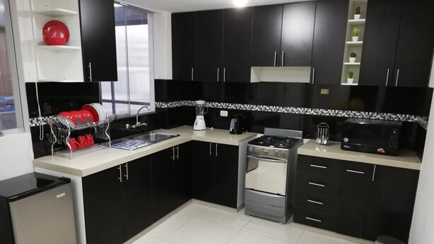 A modern kitchen with black cabinets, a white countertop, a stove, a sink, and a dishwasher. - Departamentos Arequipa Inn (Arequipa)