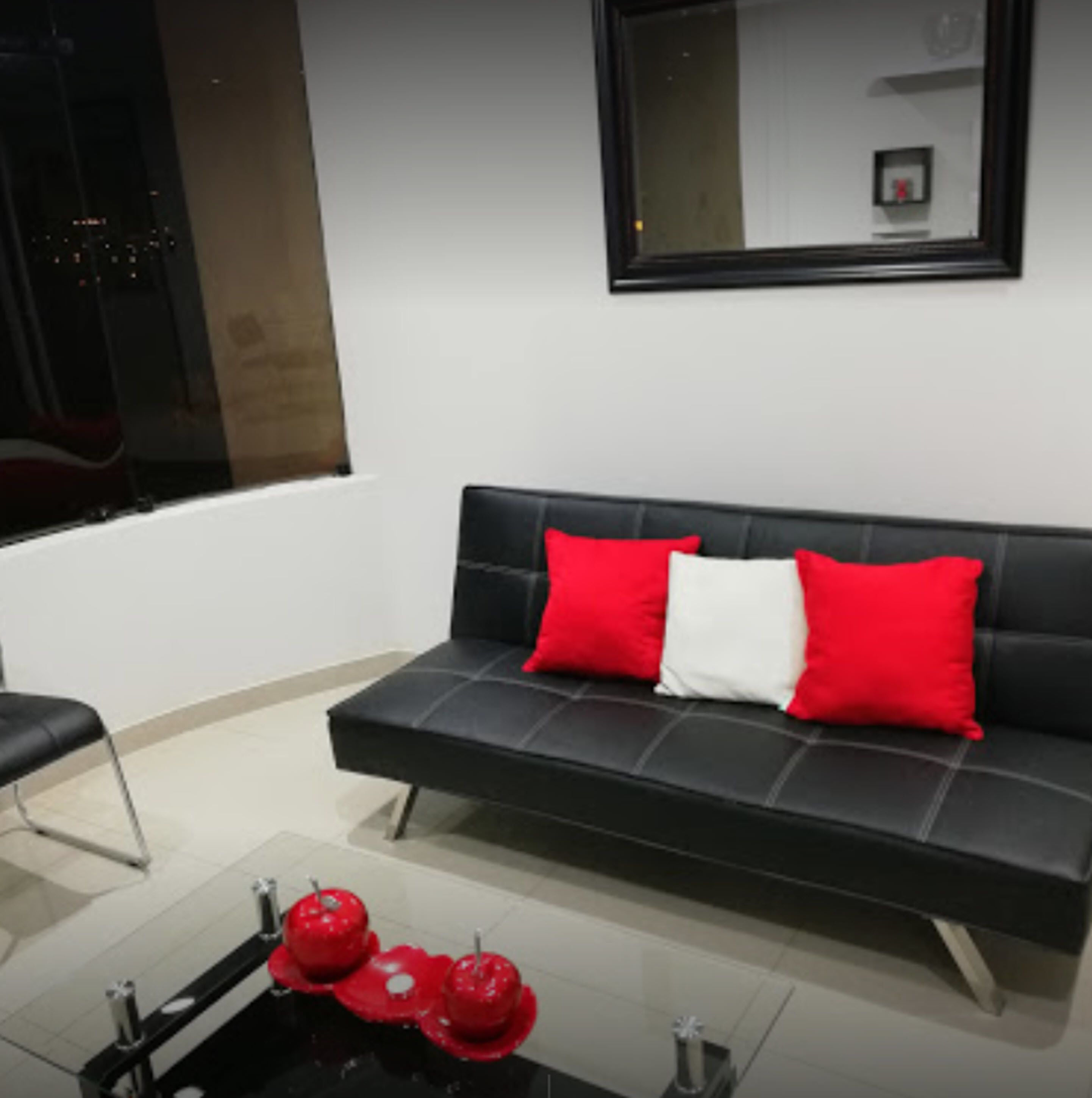 A modern living room with a black sofa, red and white cushions, and a glass coffee table with red decorative items.