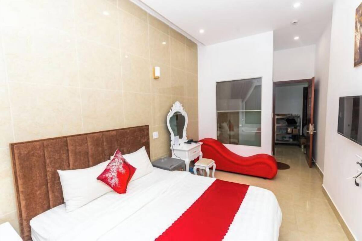 Hotelkamer met een groot bed, een kaptafel met spiegel, een rode accentmuur en een schuifdeur naar een badkamer.