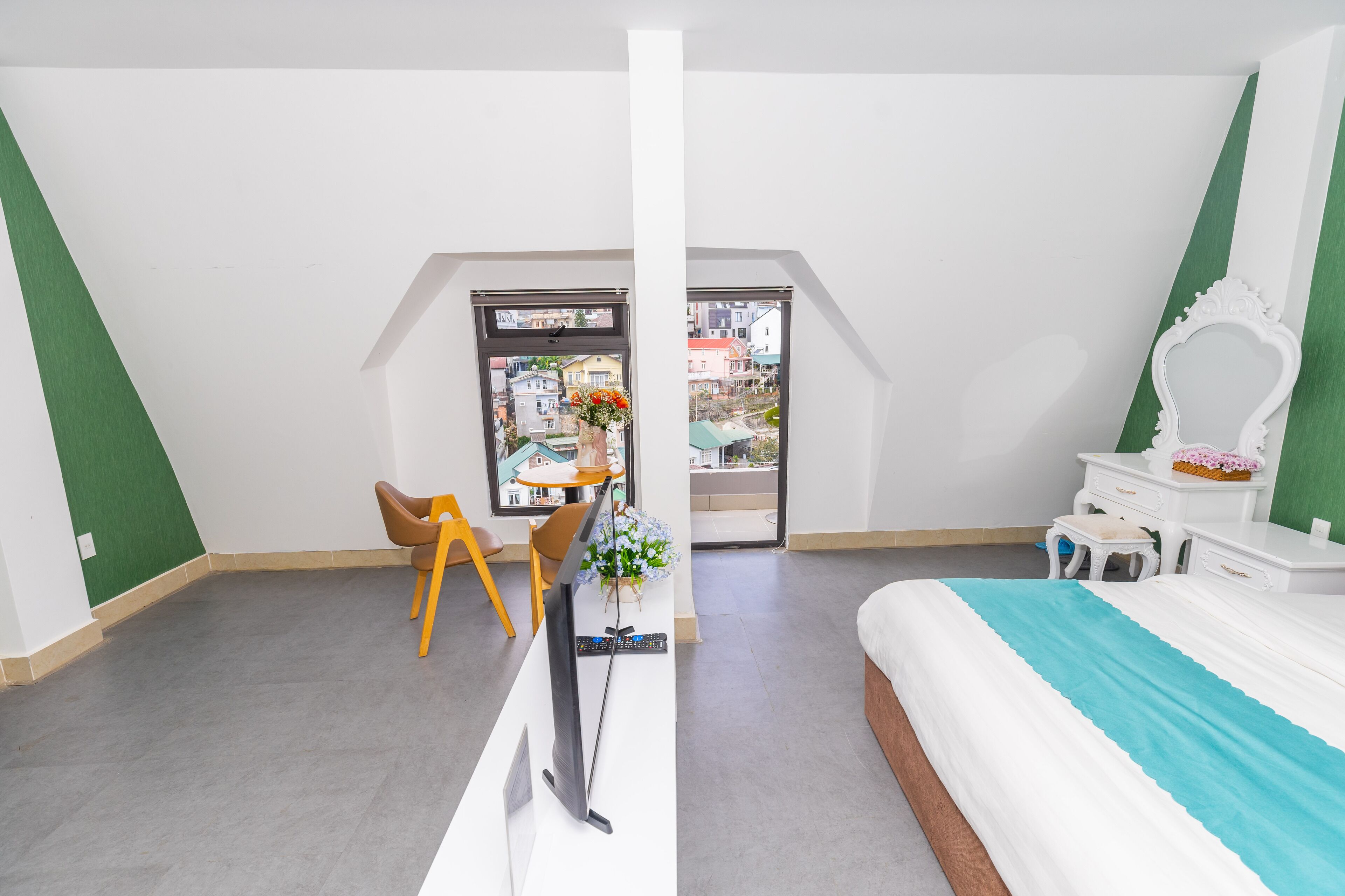 Una camera da letto con un letto, una scrivania, una sedia, una TV e una finestra con vista sugli edifici.