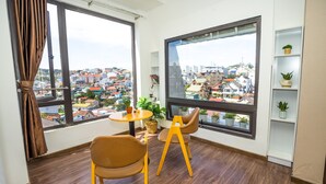 Una habitación con un ventanal grande, una pequeña mesa, dos sillas y una estantería con plantas.