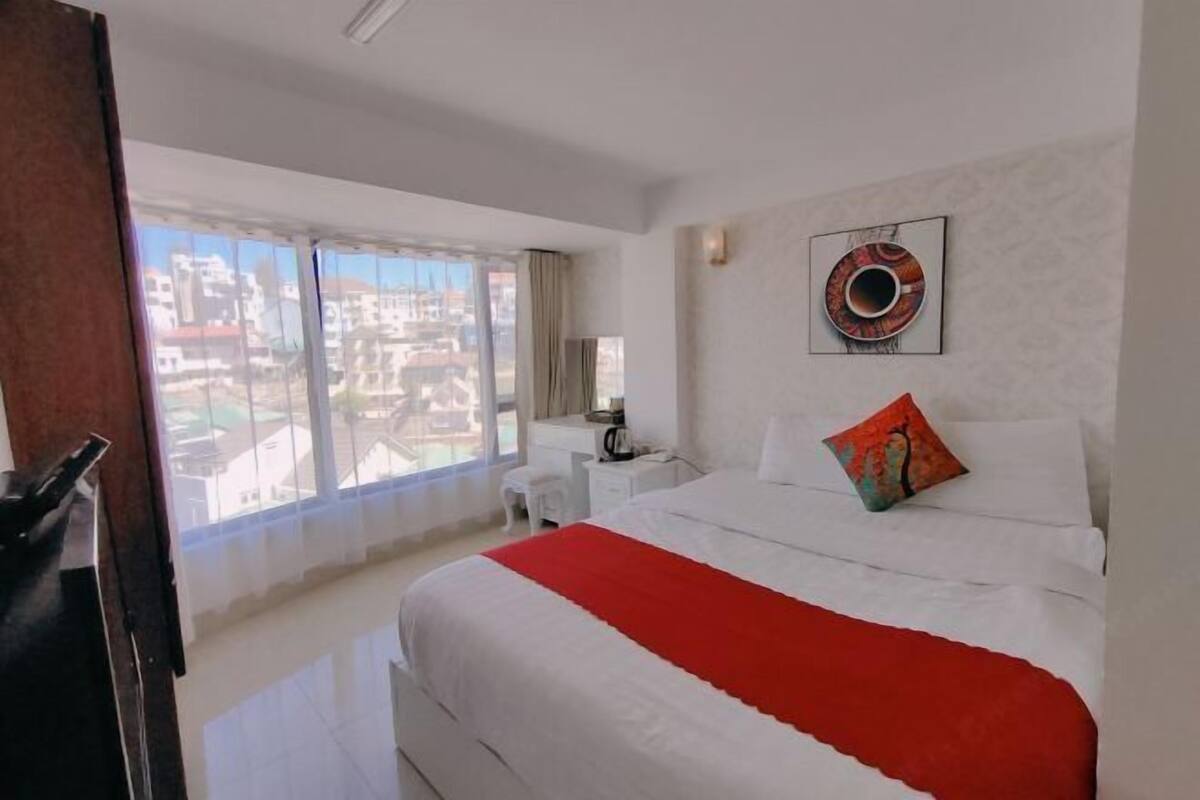 Hotelkamer met een groot bed, nachtkastje, stoel en raam met uitzicht op de stad.