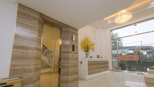 Un área de recepción con pared de mármol, mostrador de recepción, candelabro y un ventanal grande.