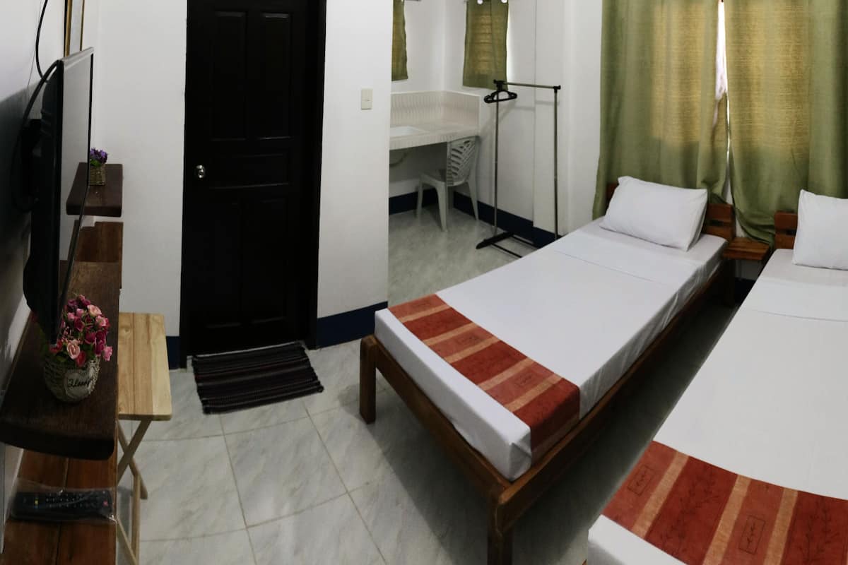 A hotel room with two single beds, a desk with a chair, a television, and a small table with a vase of flowers.