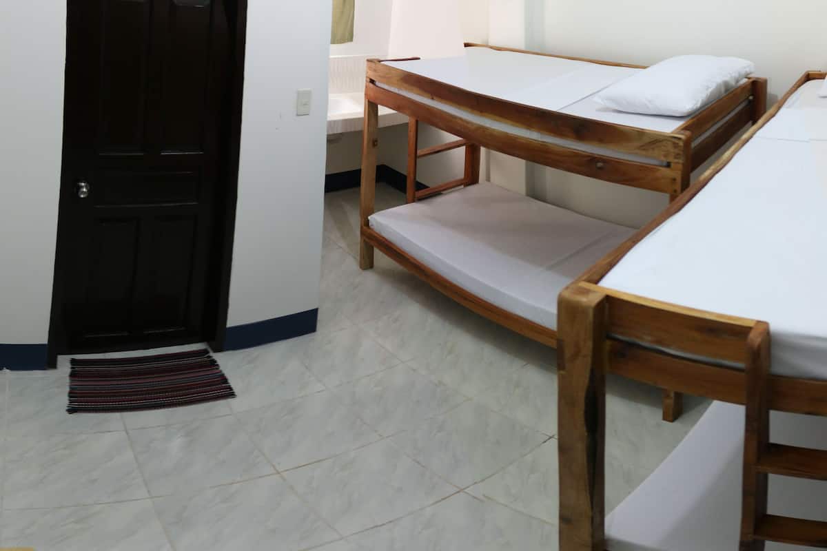 A room with two wooden bunk beds, a small table with a basket of flowers, and a door leading to a bathroom.