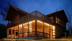 Une maison en bois à deux étages, dotée d’un balcon et de grandes fenêtres, entourée d’arbres.