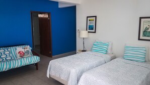 A room with two beds, a sofa, a door, and a wall with a framed picture. - Casa Piña Apartment 2 (Rincon)