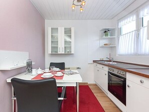 Une cuisine de taille réduite avec des meubles blancs, un tapis rouge et un coin repas comprenant une table et des chaises.