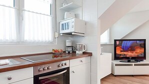 A modern kitchen with white cabinetry, a microwave, a coffee maker, and a television on a stand. - Vacation apartment 4 - House Ankerplatz (Esens)