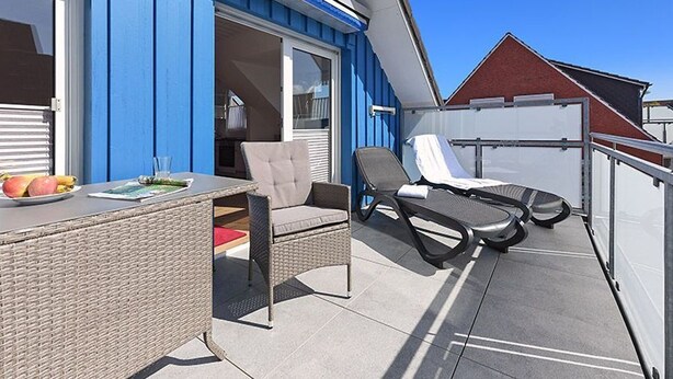 An outdoor balcony with a wicker table, two lounge chairs, and a red cushion. - Vacation apartment 4 - House Ankerplatz (Esens)