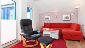 A modern living room with a black leather chair, a red sofa, and a white coffee table. - Vacation apartment 4 - House Ankerplatz (Esens)