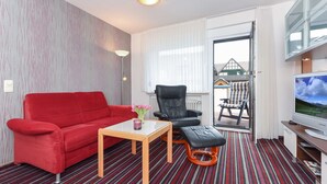 Hotellihuone, jossa on punainen sohva, musta nahkainen nojatuoli, pieni puinen pöytä ja televisio.