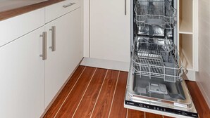 Keittiössä on valkoiset kaapit, puinen työtaso, Bosch-merkkinen astianpesukone ja ikkuna tiskialtaan yläpuolella.