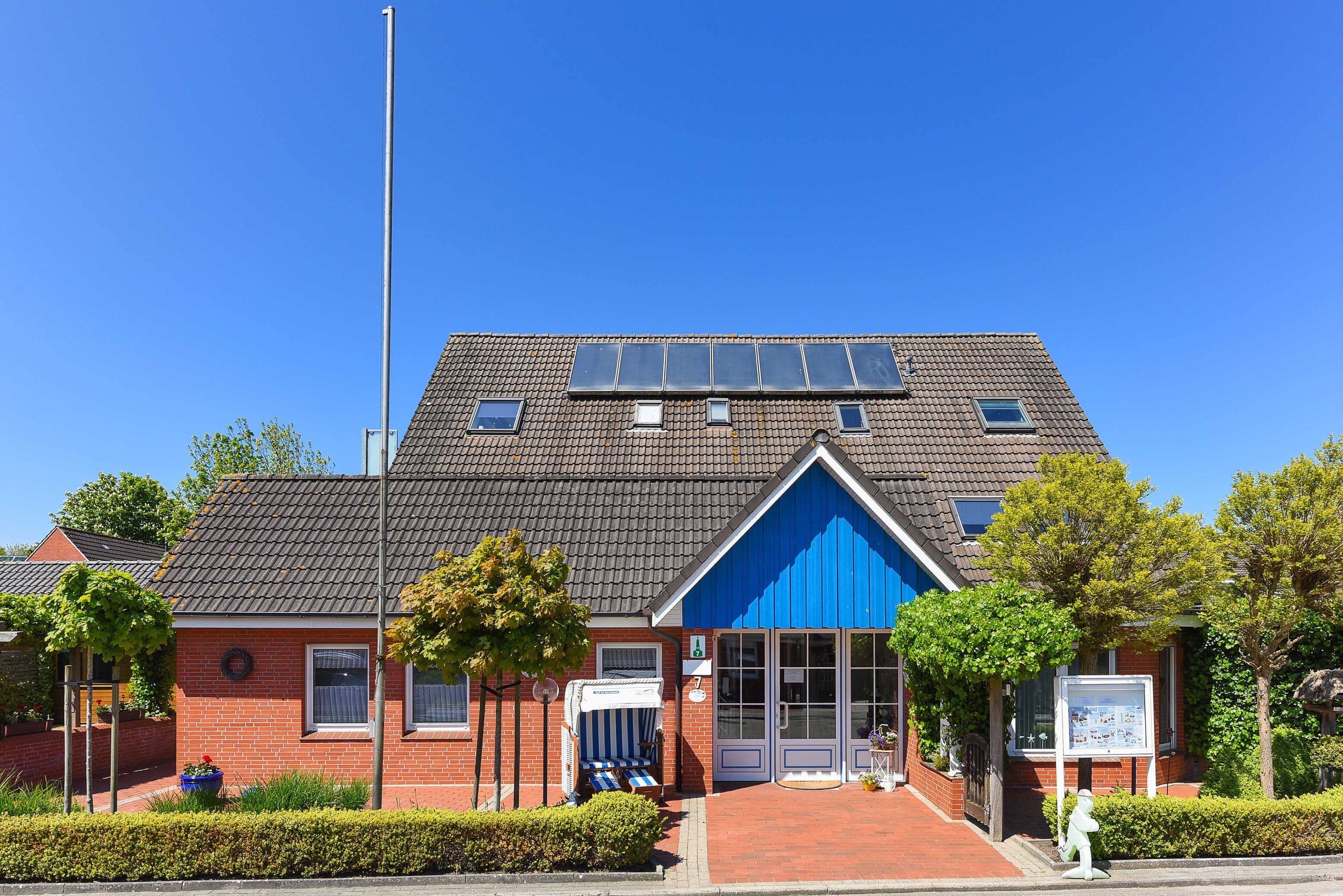 Een roodbruik gebouw met een blauwe gevel, zonnepanelen en een kleine tuin.