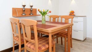 Een eethoek met een houten tafel en stoelen, een vaas met bloemen en een fruitschaal op de tafel.