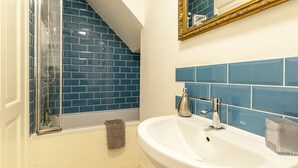 Une salle de bain avec un lavabo blanc, des murs recouverts de carreaux bleus, une douche en verre et une serviette beige.