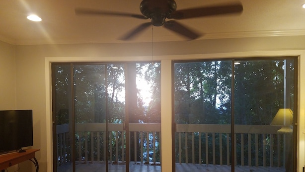 A room with a ceiling fan, a TV on a wooden stand, and large sliding glass doors leading to a deck with a wooden railing. - 2/2 condo daphne Al. (Daphne)