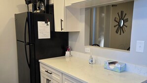 A kitchen with white cabinets, a black refrigerator, a marble countertop, and a wall clock. - 2/2 condo daphne Al. (Daphne)